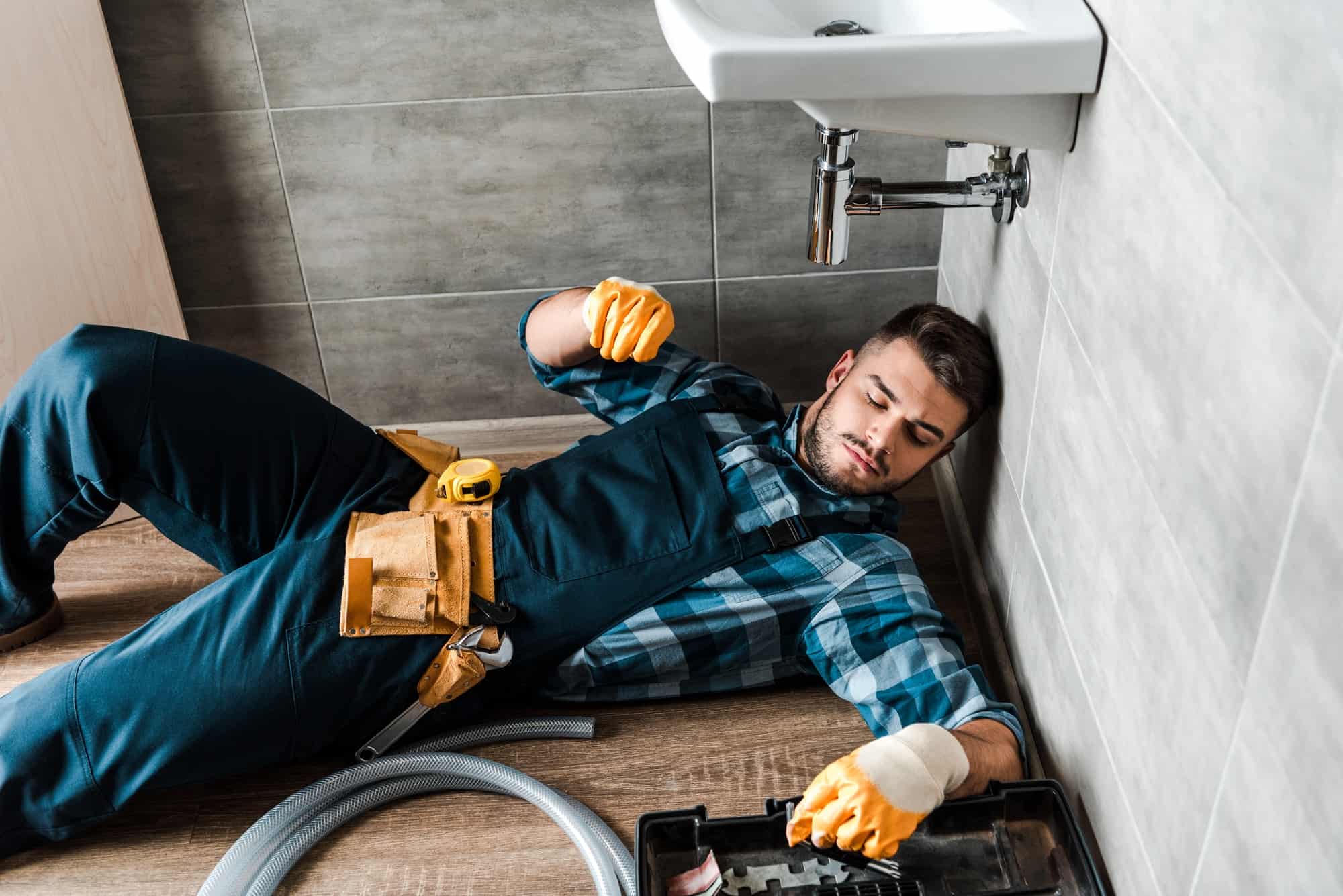 bearded handyman lying on floor near toolbox in bathroom